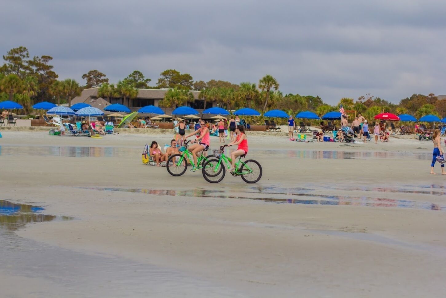 A beach with people, some on bicycles, and beach umbrellas in the background.
