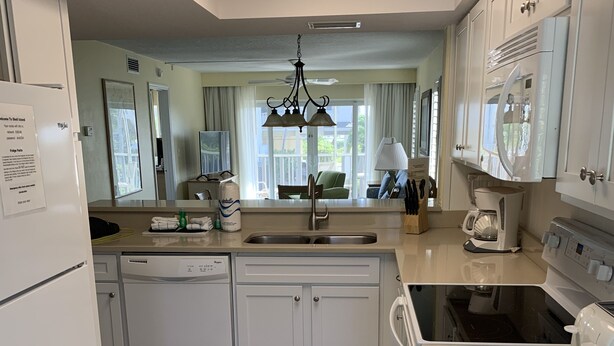 A modern kitchen with white cabinetry, a central island, a built-in oven, and a coffee maker. - Wonderful Sanibel Island condo. 2 bed 2 bath. Sleeps 6. Weekly rental.  (Sanibel)