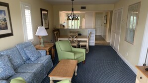 A cozy living room with a sofa, two armchairs, a coffee table, and a lamp. A kitchen area is visible in the background with a dining table and chairs. - Wonderful Sanibel Island condo. 2 bed 2 bath. Sleeps 6. Weekly rental.  (Sanibel)