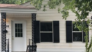 Una casa de un piso con fachada blanca y contraventanas negras, puerta principal y un pequeño porche con escalones.