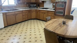 Cozinha com armários de madeira, micro-ondas, forno e mesa de jantar com cadeiras.