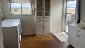 Uma lavanderia com máquina de lavar, armário com gavetas, janela com vista para um campo e porta que dá para o exterior.