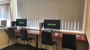 Laboratório de informática com dois monitores, quatro cadeiras e uma janela com persianas.