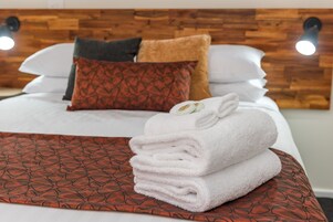 Una cama bien hecha con un edredón estampado, una pila de toallas dobladas y una variedad de almohadas.