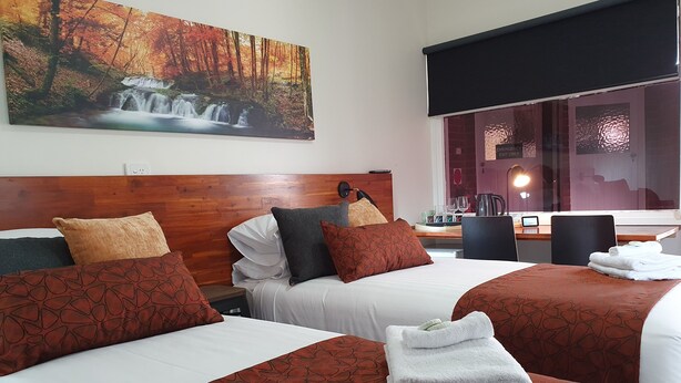 Quarto de hotel com duas camas, cabeceira de madeira, pintura de uma cascata e vista para uma área de spa.