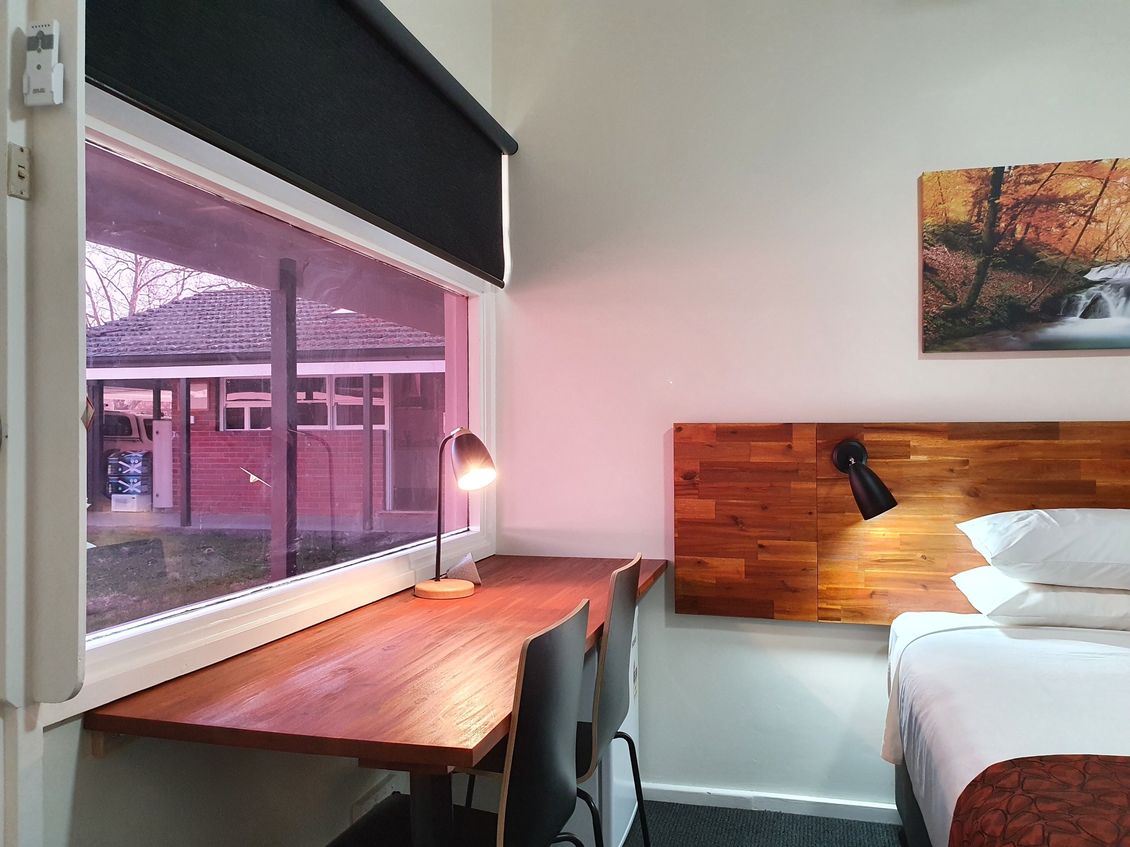 A hotel room with a wooden desk, a bed, and a window with a view of a building outside.