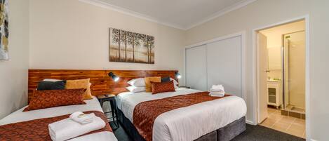 Une chambre d’hôtel avec deux lits, une tête de lit en bois, un tableau accroché au mur et un espace douche visible à travers une porte ouverte.