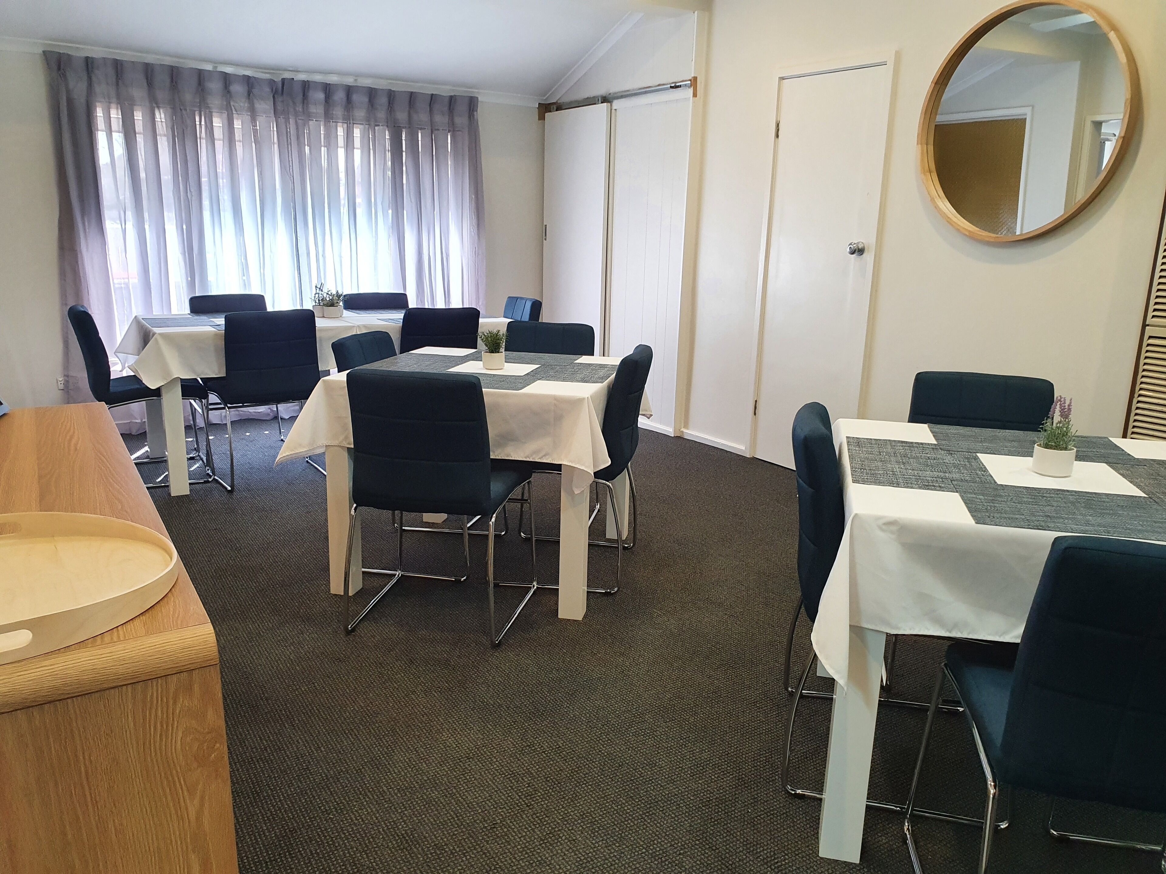 A hotel conference room with tables and chairs, a large mirror, and a view through the window.