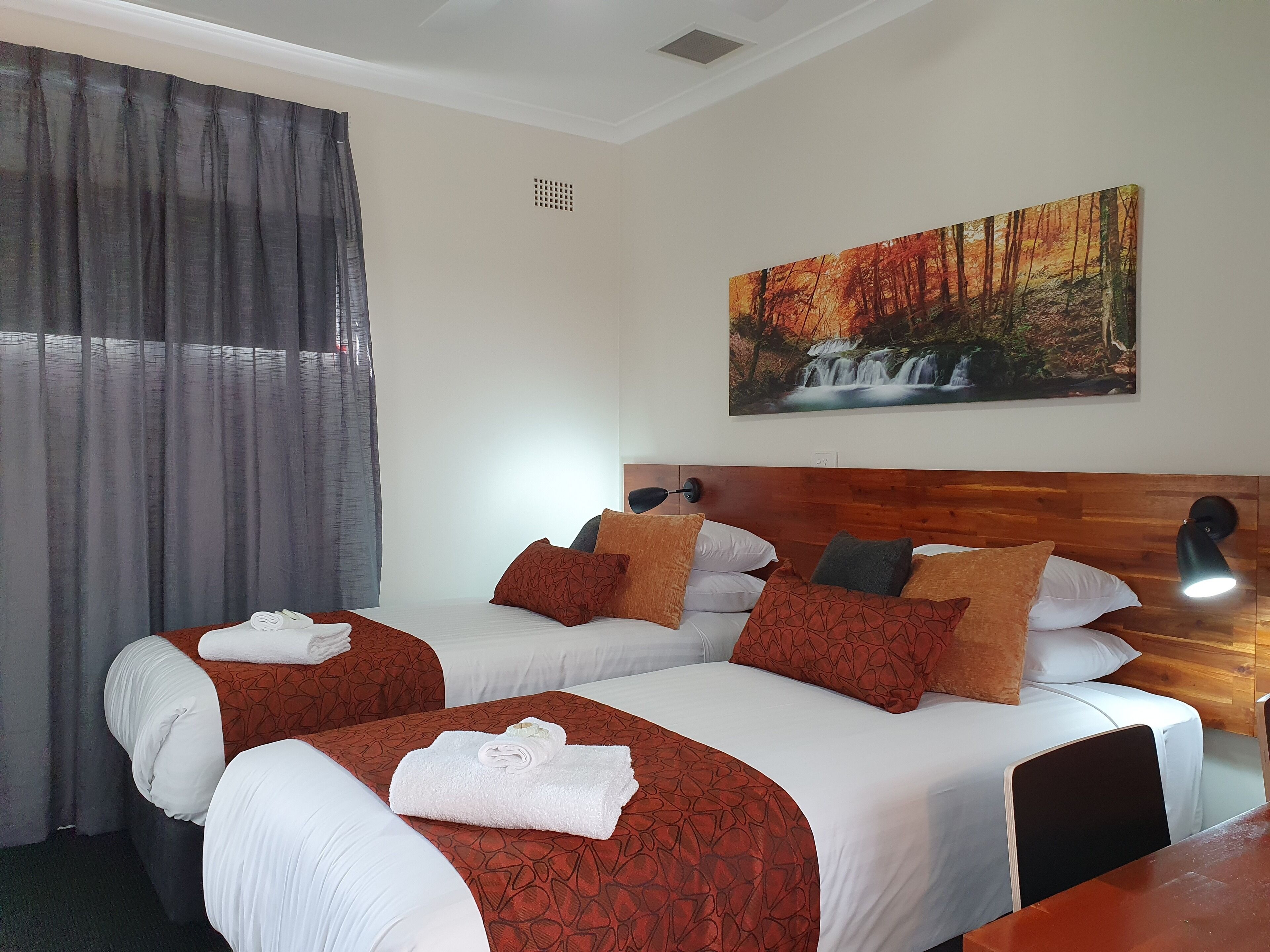 Een hotelkamer met twee bedden, een schilderij van een waterval in een bos aan de muur, en een houten hoofdbord.