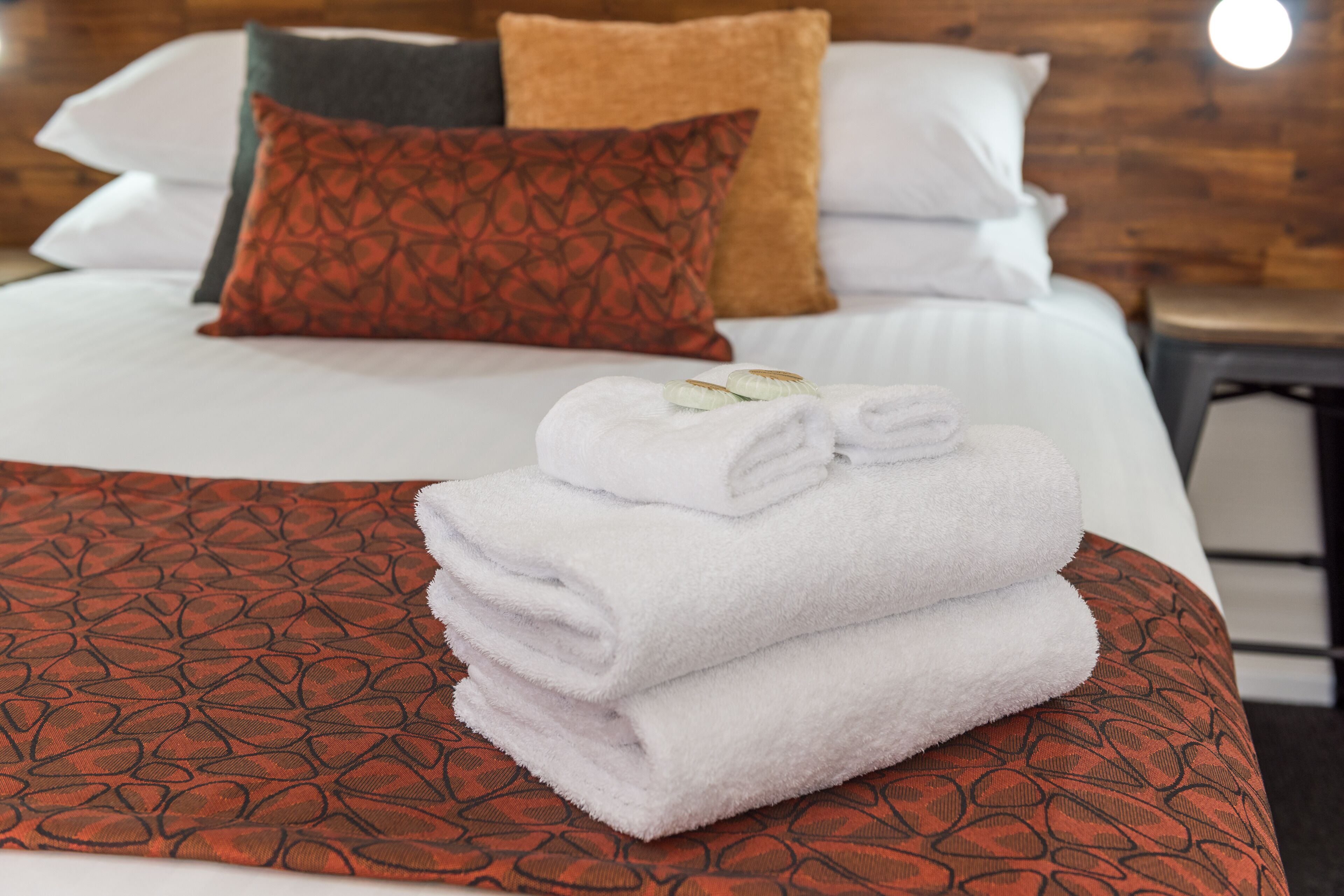 A neatly made bed with a patterned bedspread, a stack of white towels, and multiple pillows.