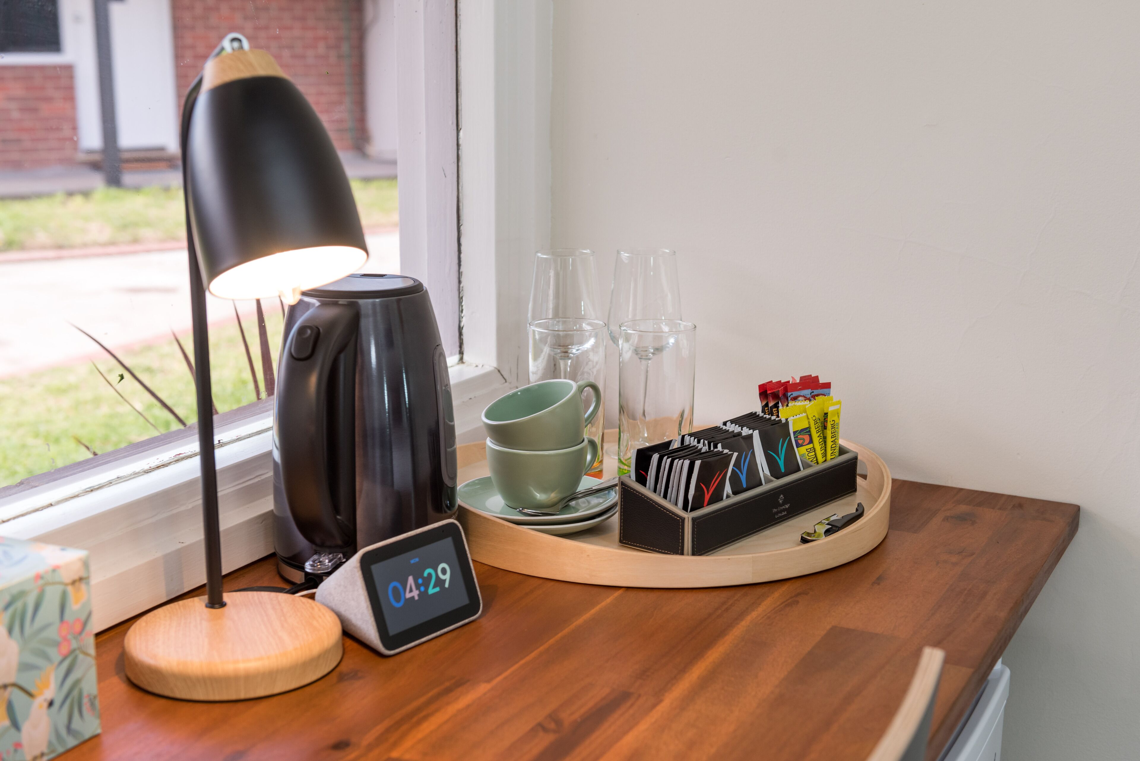 A wooden table with a coffee maker, a clock, two cups, and a tray with cards and pens.