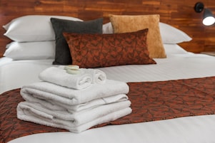 Una cama bien hecha con sábanas blancas y una pila de toallas dobladas.