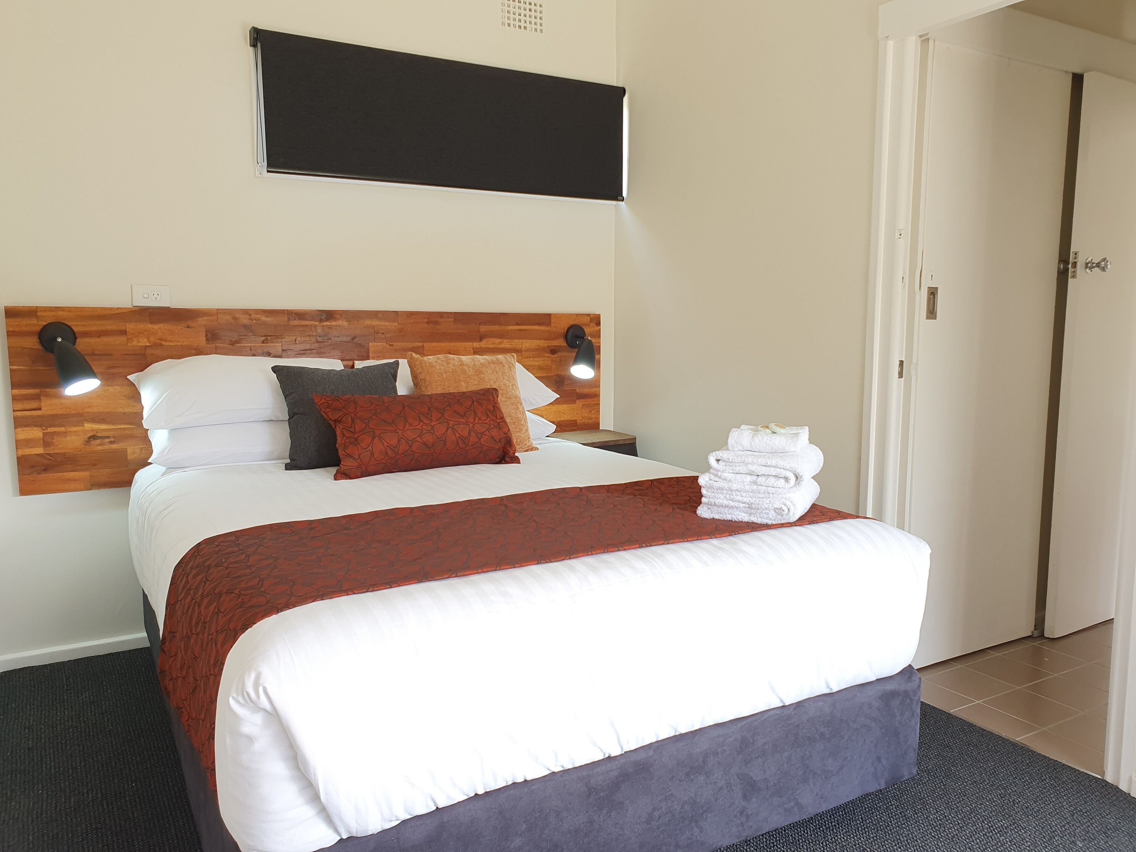 A neatly made bed with a wooden headboard, multiple pillows, and a stack of towels.