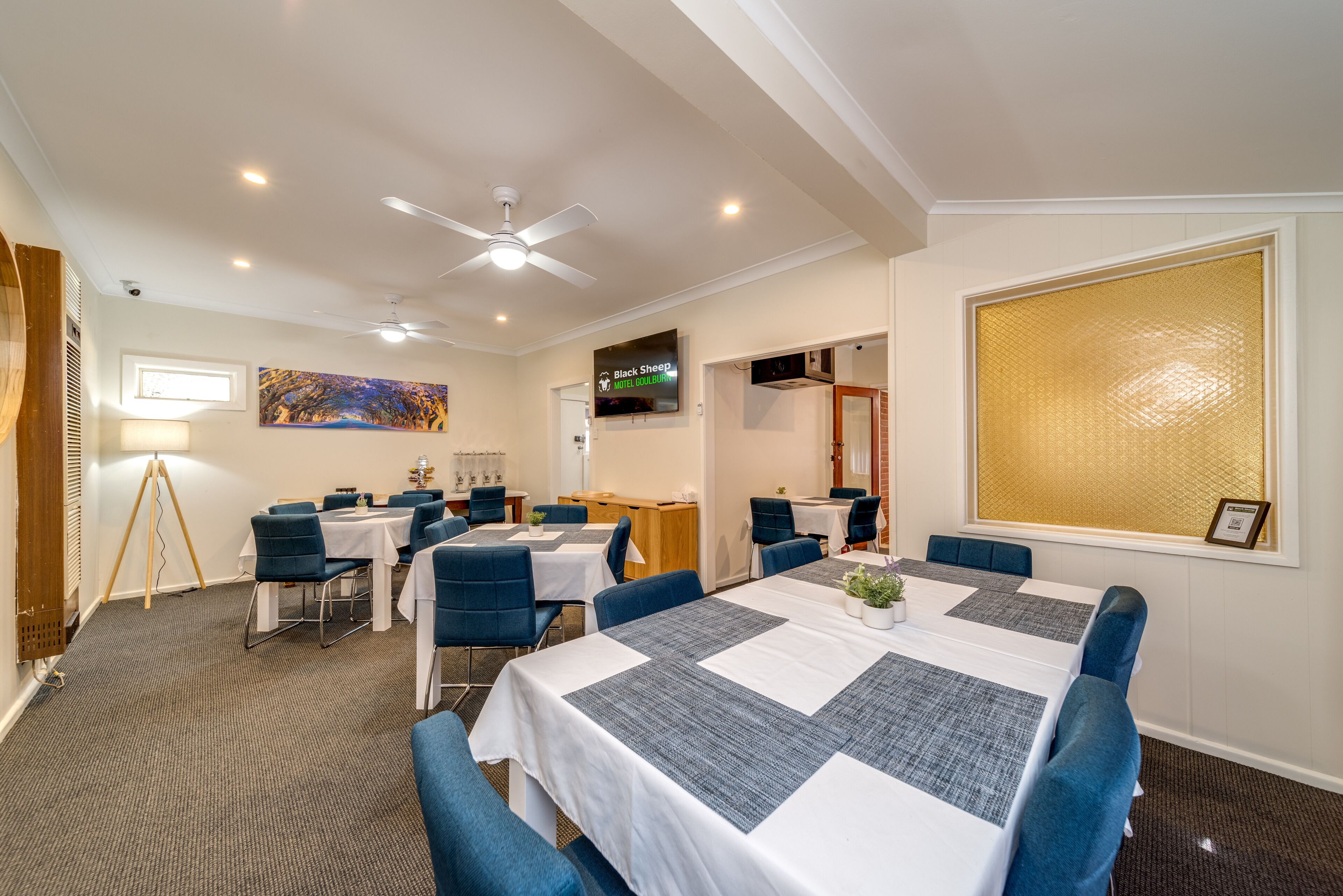 Uma sala de conferências de hotel com uma mesa grande, cadeiras azuis, um ventilador de teto e uma pintura na parede.
