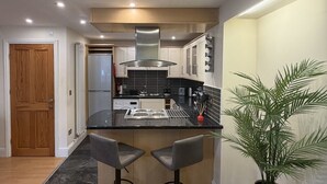 Een moderne keuken met een centraal eiland, twee barkrukken, een potplant en een houten deur.