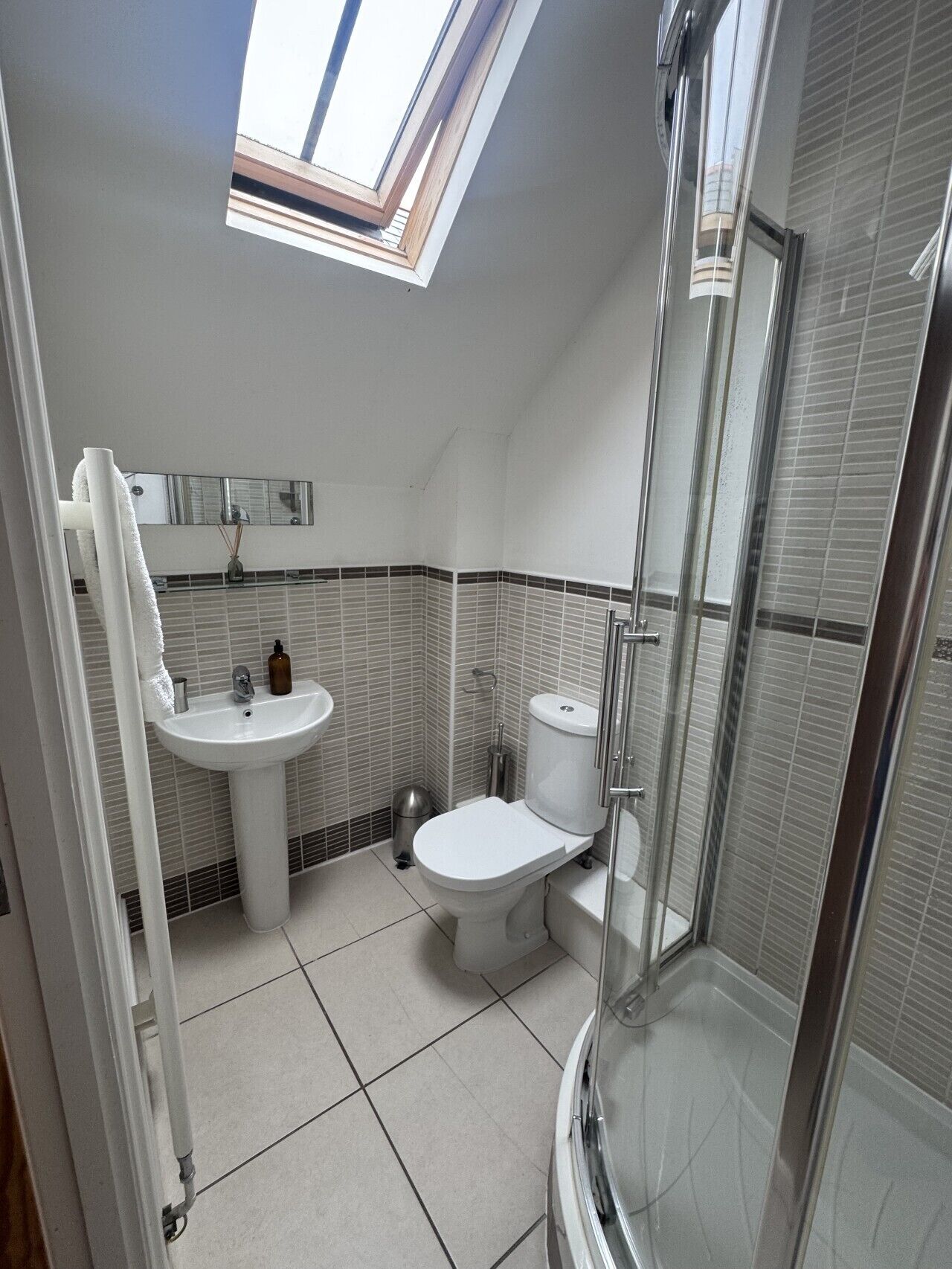 Ein modernes Badezimmer mit Dachfenster, Toilette, Waschbecken und Dusche.