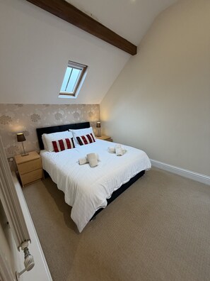 A bedroom with a skylight, a bed with white bedding and red pillows, a nightstand with a lamp, and a carpeted floor. - The Old Pump House -Tenby (Pembrokeshire)