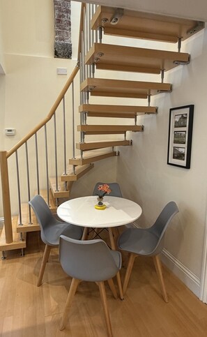 A modern interior with a spiral staircase, a round dining table with chairs, and a small decorative item on the table. - The Old Pump House -Tenby (Pembrokeshire)