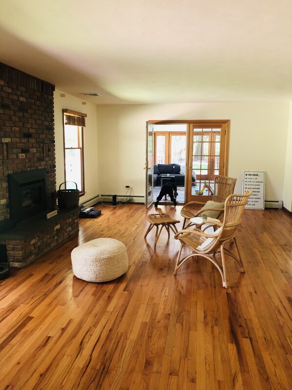 A living room with a brick fireplace, wicker furniture, and a view through glass doors to an outdoor area.