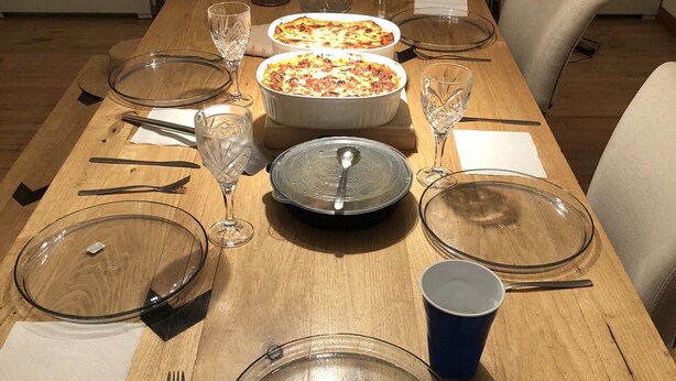 Et spisebord dækket med klare glas, tallerkener og en blå kop, med en vase med tørrede blomster i midten.