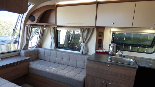Een compact RV-interieur met een kitchenette, zithoek en een raam met gordijnen.