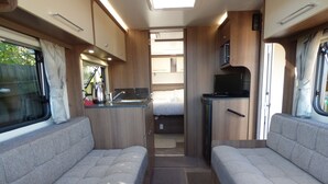 Een compact camperinterieur met twee zithoeken, een kitchenette en een klein slaapgedeelte.