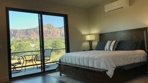 A bedroom with a large bed, a nightstand with a lamp, and a view of a mountainous landscape through a sliding door.