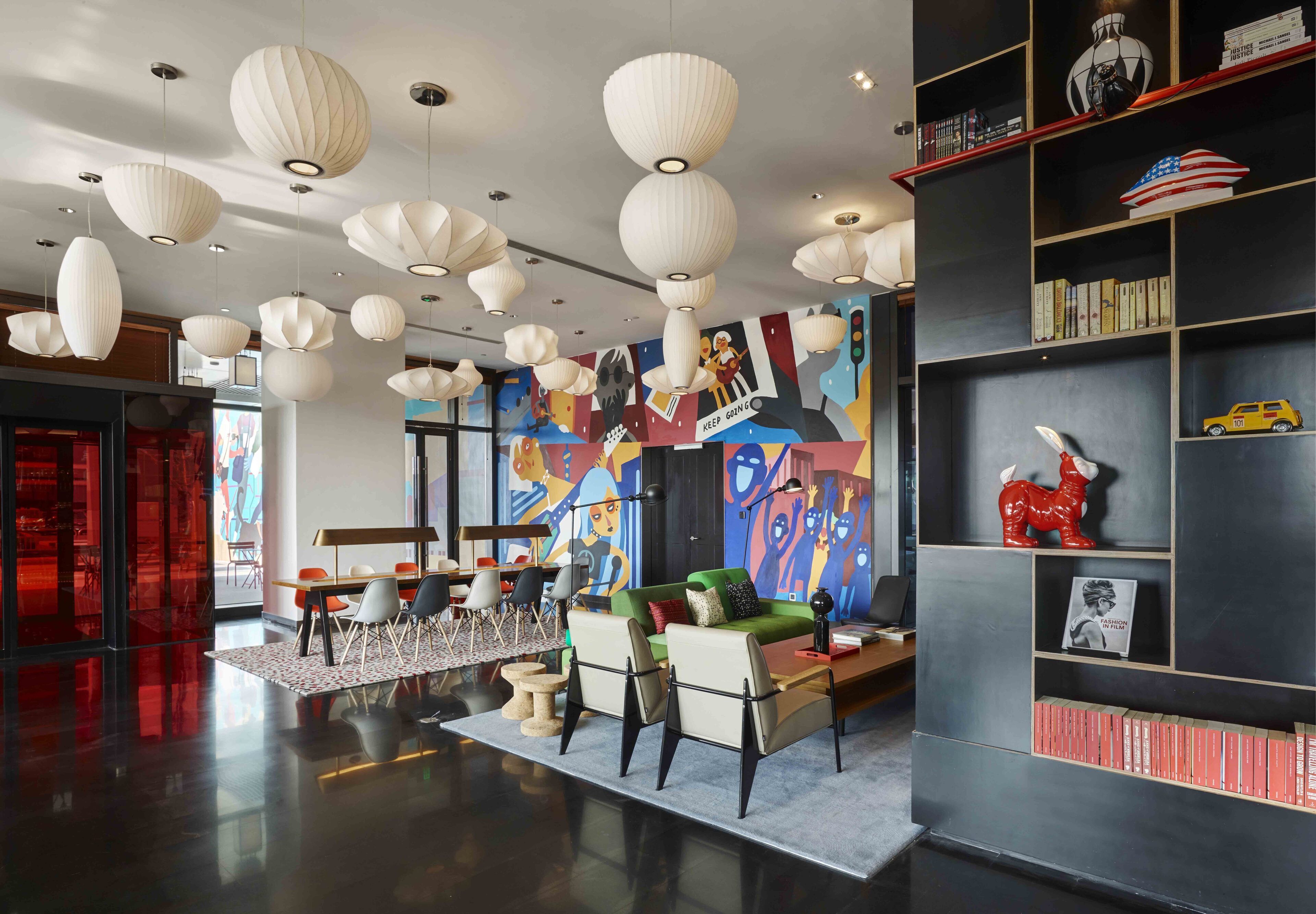 Een modern interieur met een bank, stoelen, een boekenkast en hangende lampen.