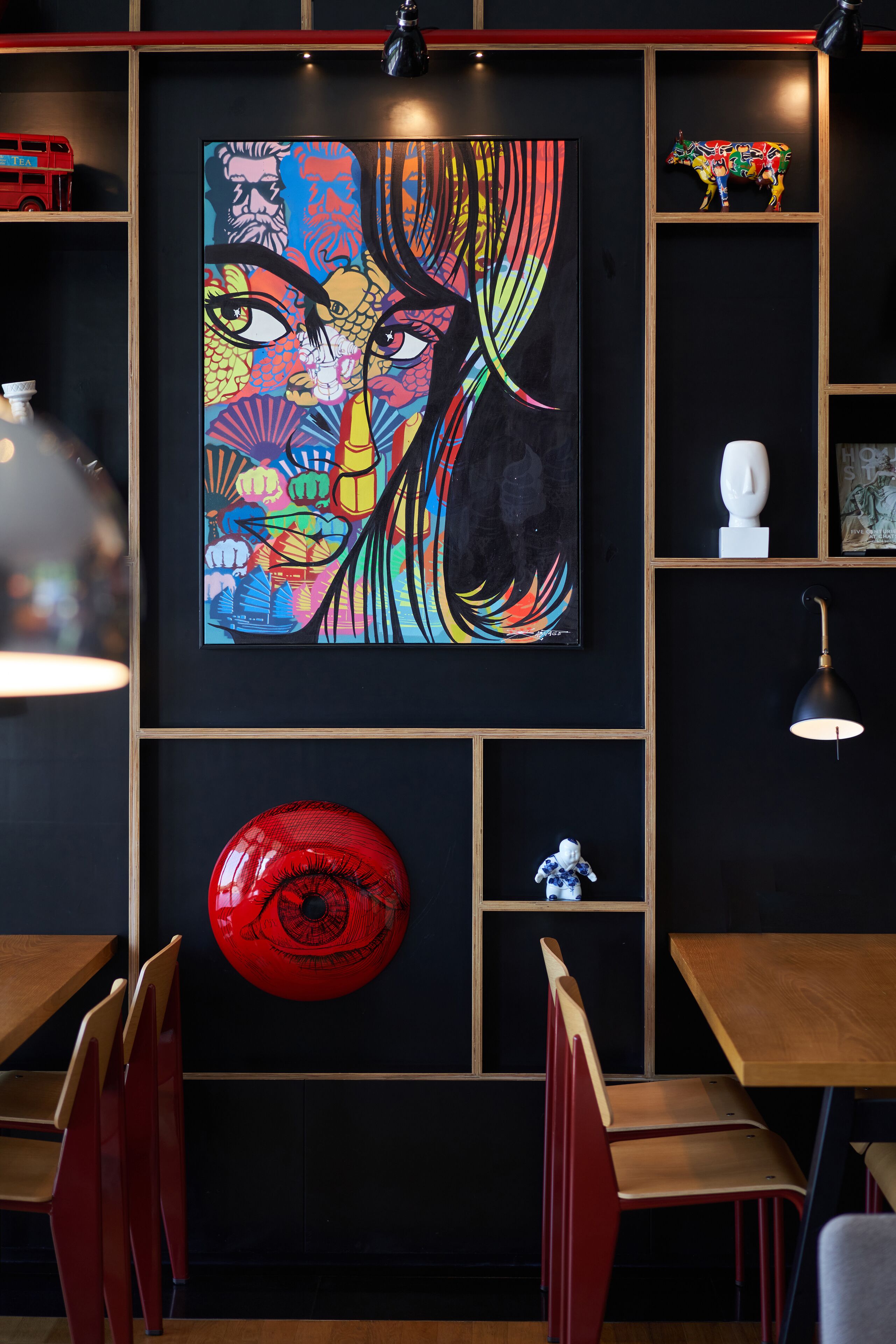 Un intérieur moderne agrémenté d’un grand tableau abstrait aux couleurs vives, de meubles en bois et d’un objet circulaire rouge accroché au mur.