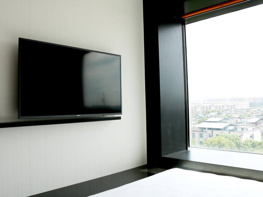 Een moderne kamer met een flatscreen televisie aan de muur, een groot raam met uitzicht op de stad en een minimalistisch design.