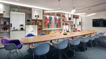 Une salle de réunion moderne, dotée d’une longue table en bois, de chaises colorées et d’un grand tableau abstrait accroché au mur.