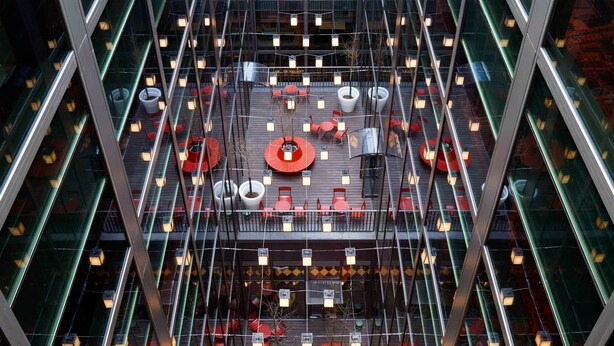Een modern gebouw met een glazen gevel, meerdere verdiepingen en een centraal atrium met zitgedeeltes en plantenbakken.