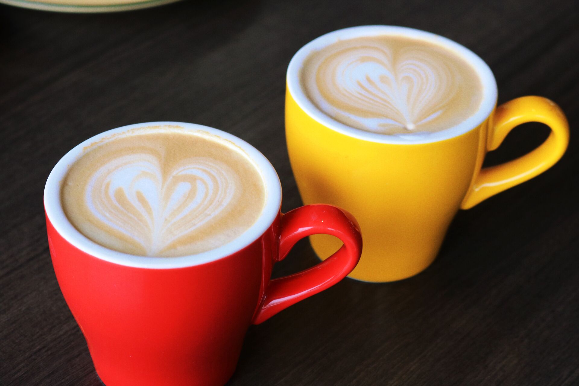 Two cups of coffee with heart-shaped latte art on a wooden table.