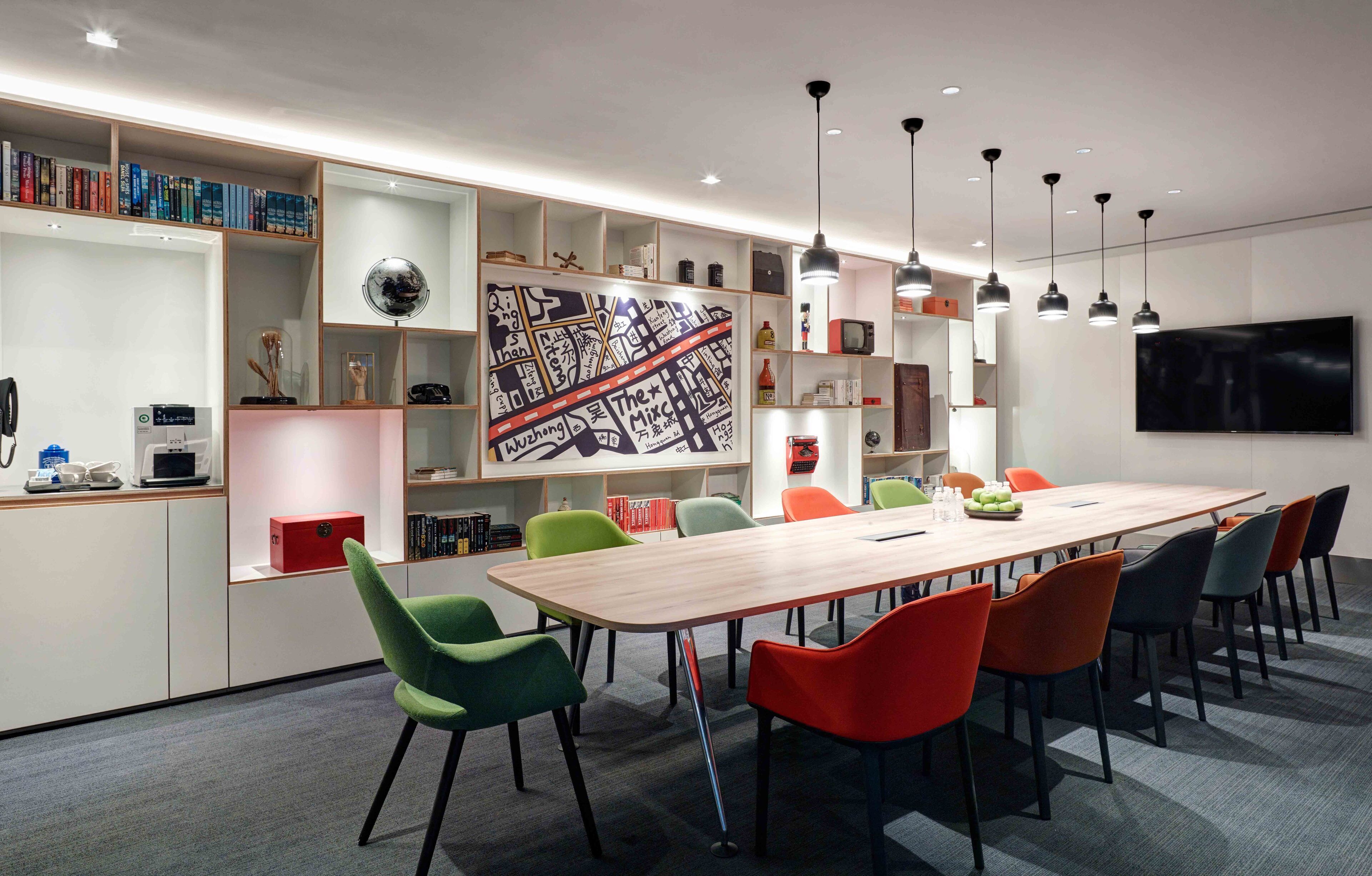 A modern meeting room with a long table, colorful chairs, and a large map on the wall.