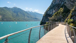 A wooden boardwalk leading to a coastal area with clear turquoise water and sailboats. - Rustichel fantastic Lake View, Toscolano Maderno, Italy (Toscolano Maderno)