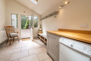 A kitchen with a wooden countertop, a built-in dishwasher, and a chair with a cushion. - Alexander House, Thorpeness (Leiston)