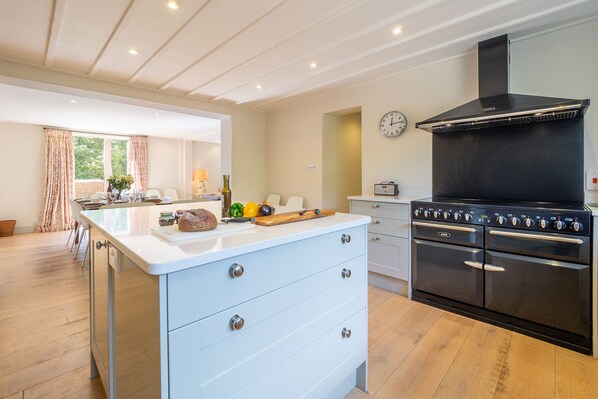 A modern kitchen with a central island, double ovens, and a large window with curtains. - Alexander House, Thorpeness (Leiston)