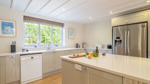 Una cocina moderna con lavavajillas integrado, un refrigerador de acero inoxidable grande y una ventana con vista a follaje.