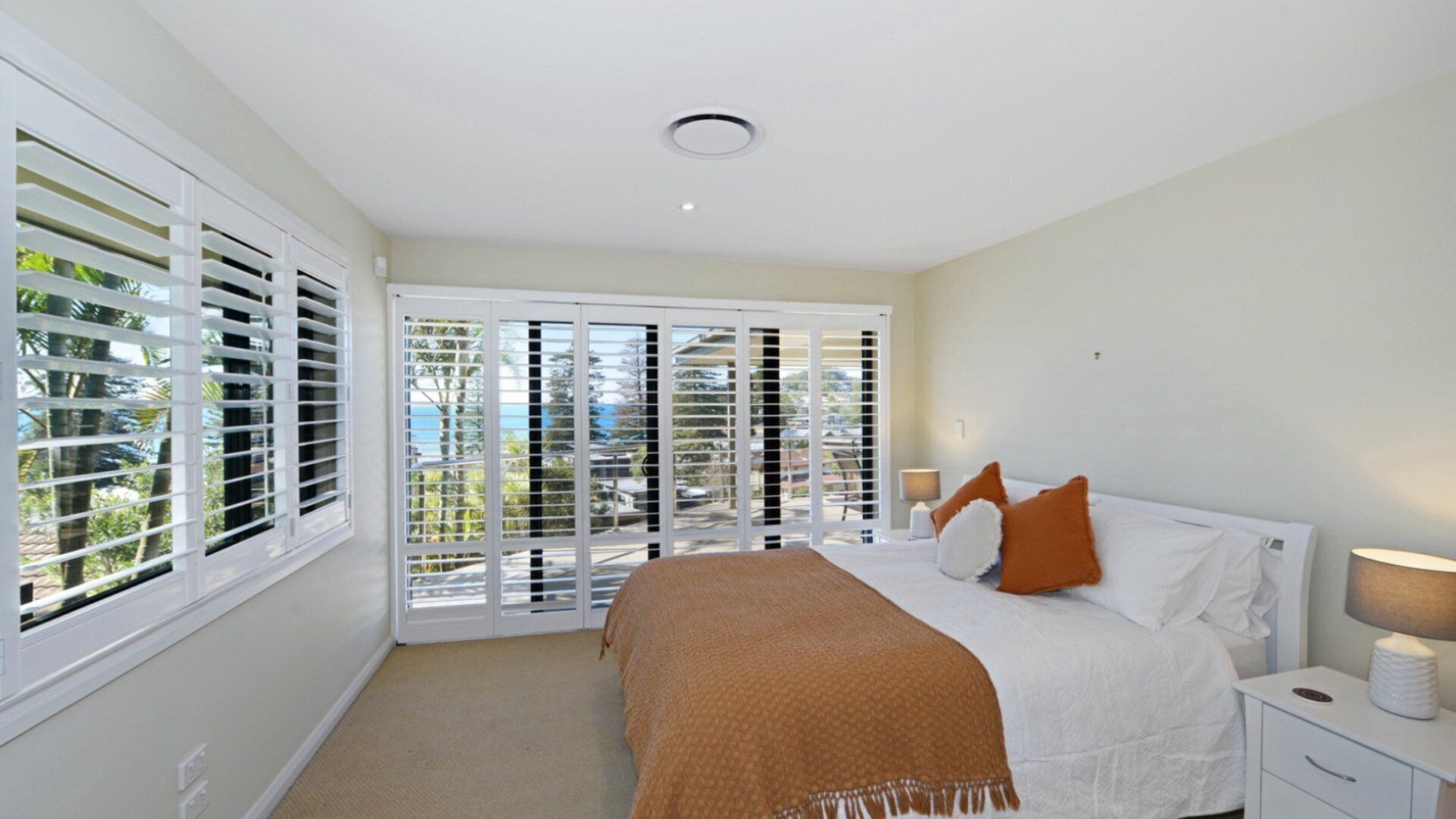 A bedroom with a bed, white nightstands, a lamp, and a view through a sliding door.