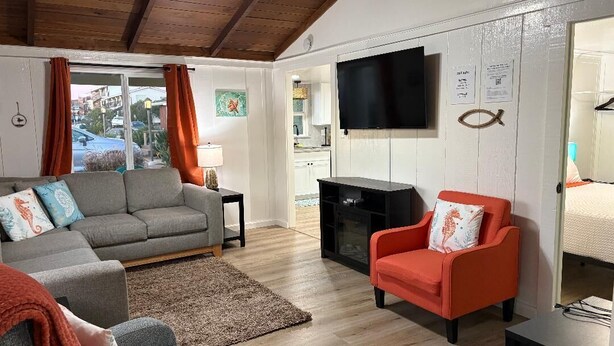 A living room with a grey sofa, a red armchair, a flat-screen TV mounted on the wall, and a wooden ceiling. - Walk to Embarcadero + Kids Dream Yard + Pool Table (Morro Bay)