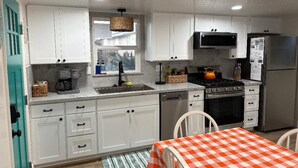 A kitchen with white cabinets, a stove, microwave, and refrigerator. There is a window above the sink and a table with a checkered tablecloth. - Walk to Embarcadero + Kids Dream Yard + Pool Table (Morro Bay)