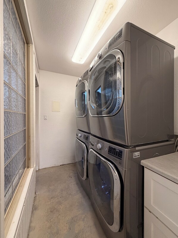 A laundry room with stacked front-loading washers and dryers, a tiled wall, and a ceiling light.