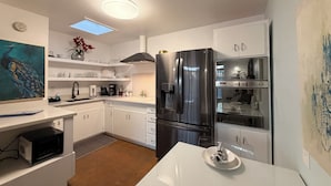 Une cuisine moderne avec des meubles blancs, un réfrigérateur en acier inoxydable, un four à micro-ondes et une table à manger avec une assiette.