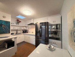 A modern kitchen with white cabinetry, a stainless steel refrigerator, a microwave, and a dining table with a plate. - 2BR Pet-Friendly Condo, Walkable Location (Phoenix)