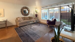 Un salon avec un canapé, une table basse et une vue sur une cour clôturée.