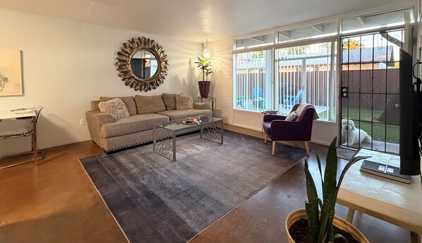 A living room with a sofa, coffee table, and a view of a fenced yard. - 2BR Pet-Friendly Condo, Walkable Location (Phoenix)