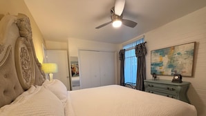 Une chambre à coucher avec un grand lit, un ventilateur de plafond, une commode, une lampe, une porte et un tableau au mur.