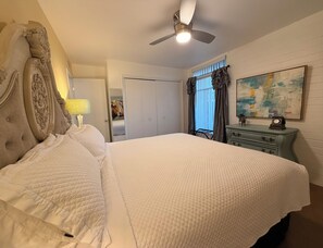 A bedroom with a large bed, a ceiling fan, a dresser, a lamp, a door, and a painting on the wall. - 2BR Pet-Friendly Condo, Walkable Location (Phoenix)