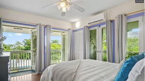 Une chambre dotée d’un grand lit, d’un ventilateur de plafond et d’un balcon offrant une vue sur la verdure.