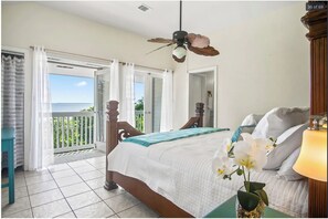 A bedroom with a bed, a ceiling fan, a balcony with a view, and a nightstand with a lamp. - Private Secluded Ocean View & Pool Near Key West (Summerland Key)